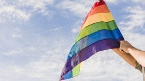 man with big flag in lgbt colors and blue sky