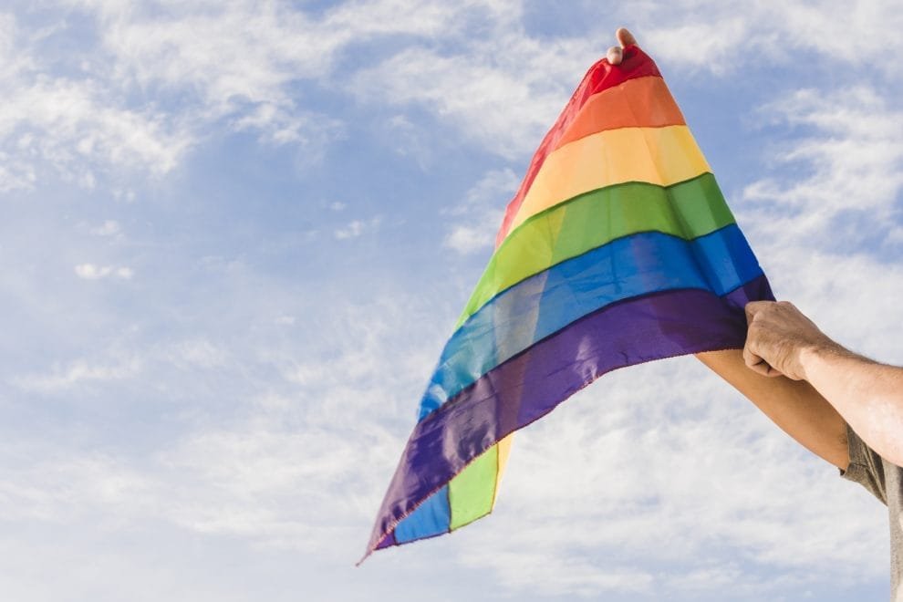 man with big flag in lgbt colors and blue sky